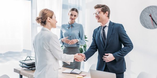 cheerful-recruiter-shaking-hands-with-woman-near-colleague-in-office.jpg