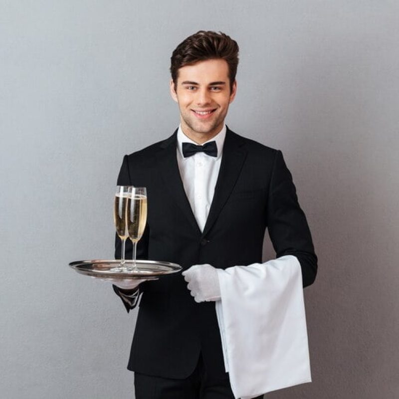 happy-young-waiter-holding-glass-champagne-towel_171337-5290